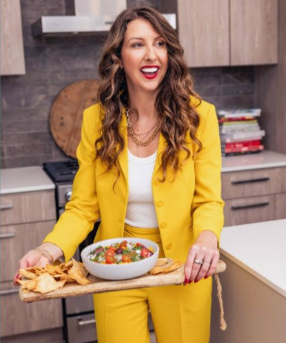 Simone Lovell in a bright yellow suit holding a bowl of fresh salad with tortilla chips